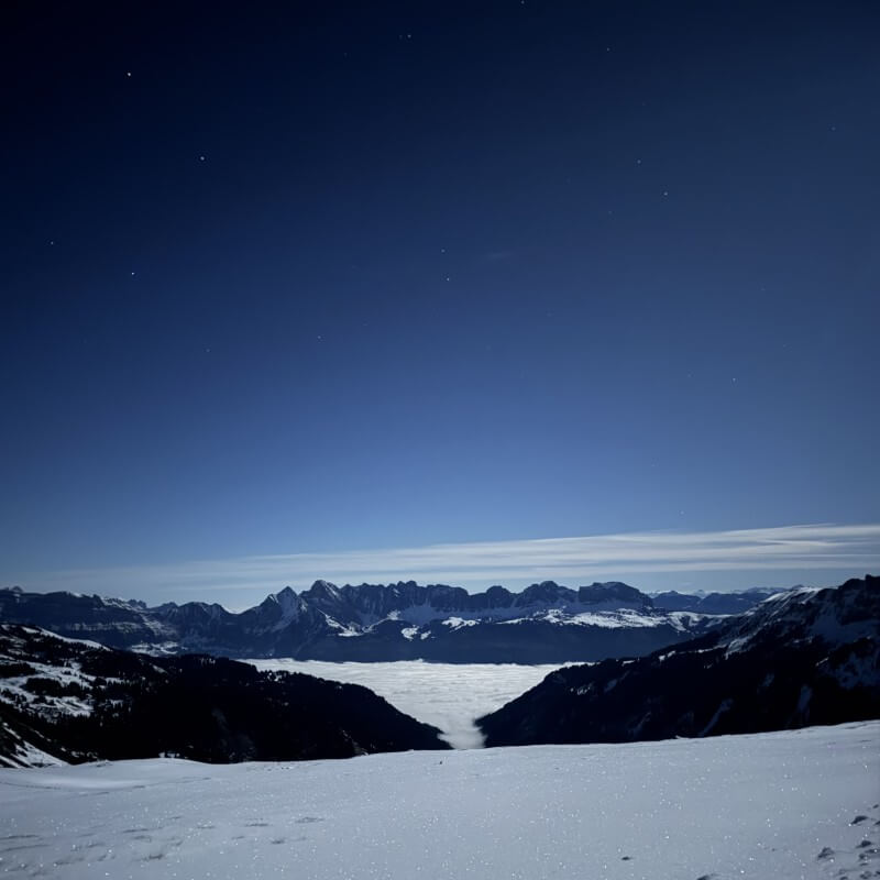 Verschneite Berglandschaft über einem Nebelmeer unter dunkelblauem Sternenhimmel.