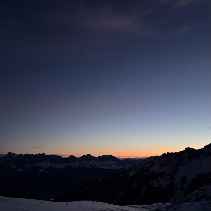 Orangefarbener Horizont hinter dunklen Bergsilhouetten unter blauem Morgenhimmel.